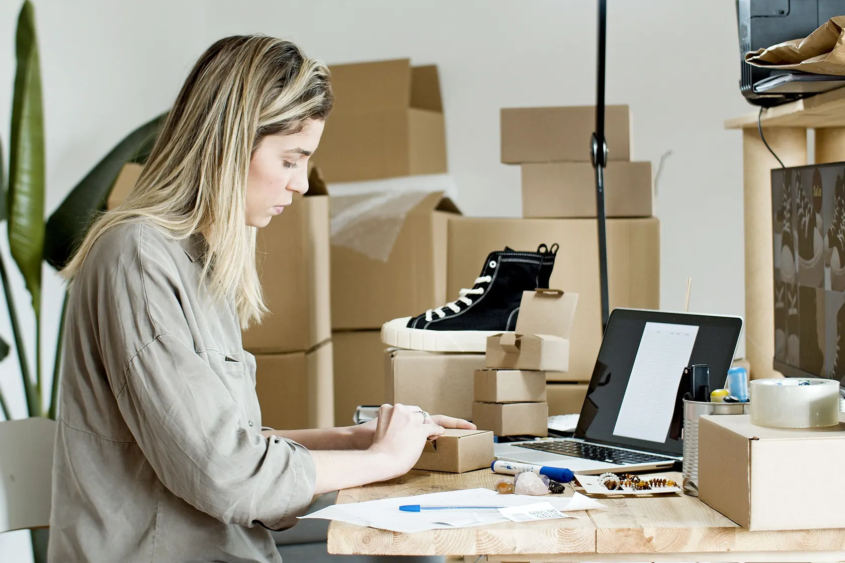 Ecommerce operator packing customer orders at a laptop with parcels and product samples